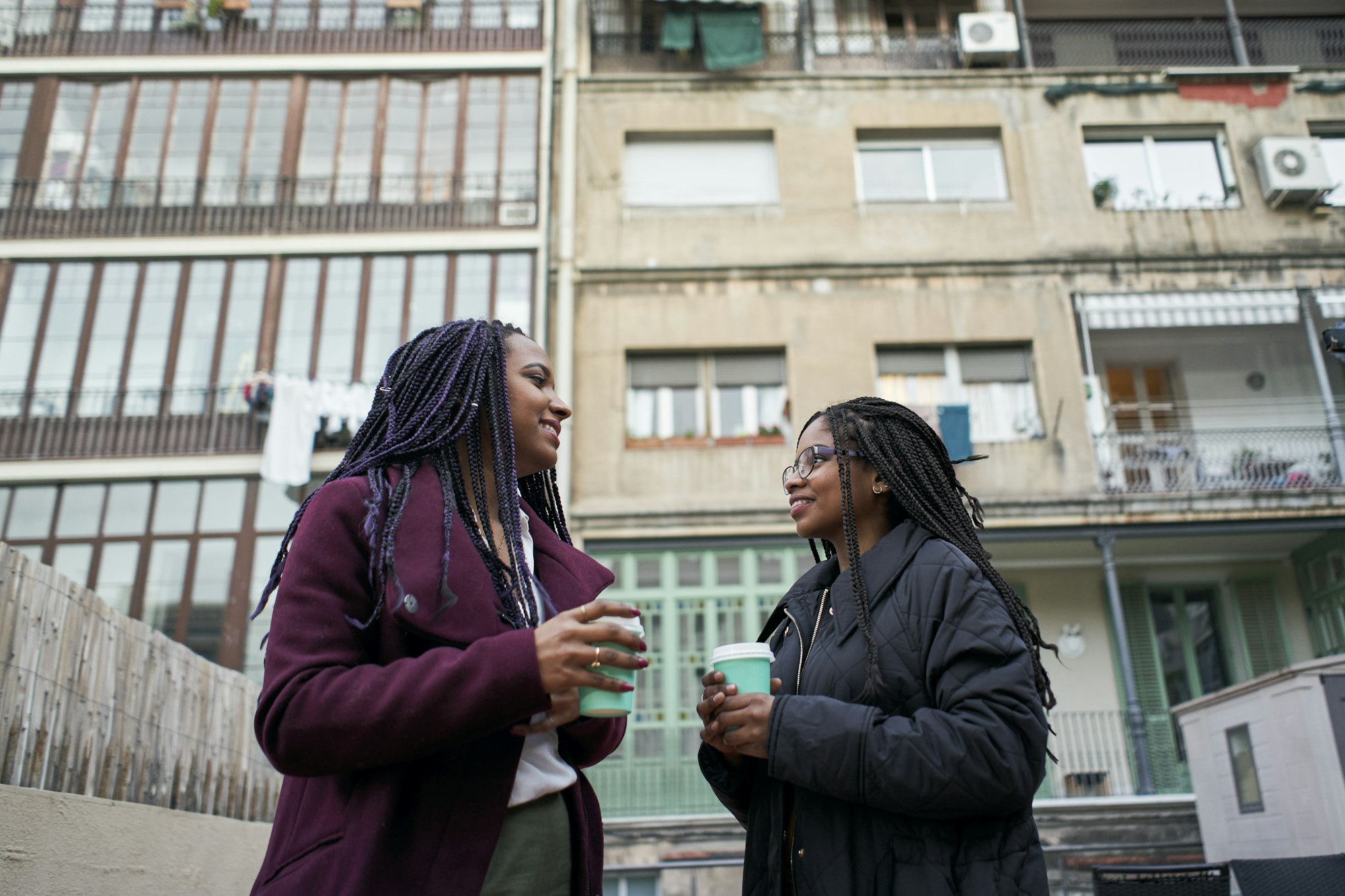 Two young African American business women using a phone and holding a coffee outside.
